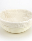 A bread proofing basket with a muslin liners sits with a white background.